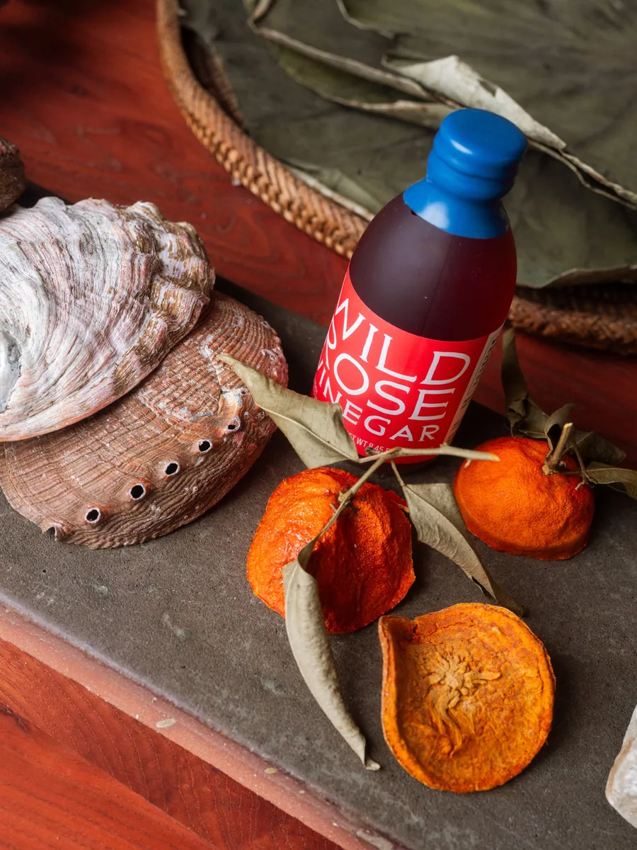A bottle of Noma Projects Wild Rose Vinegar with dried mandarins and a shell